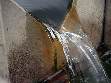 closed up on the nappe - body of water flowing over the crest - of a thin-plate v-notch weir measuring the volumetric flow of water